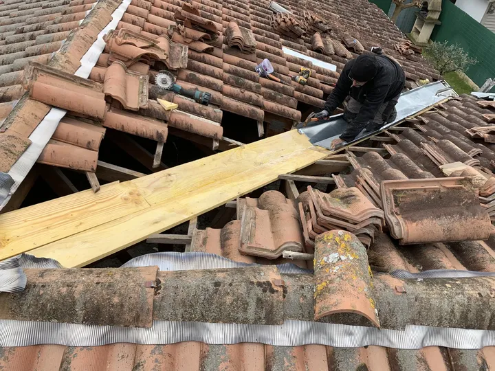 Artisan ajustant une pièce métallique dans une noue avec tuiles déposées