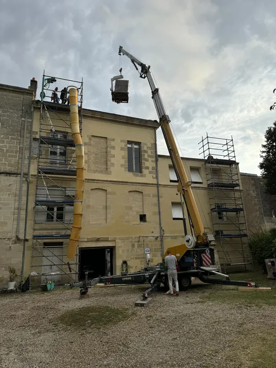 Engin de levage positionné devant un bâtiment pour un chantier en toiture
