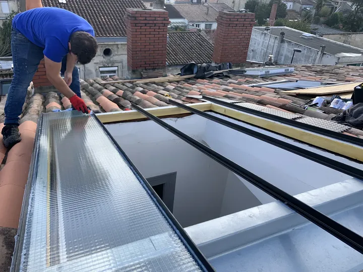 Artisan travaillant le raccord métallique le long d’une verrière en toiture