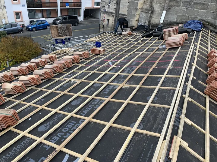 Lattage posé sur un écran de sous-toiture avec des piles de tuiles